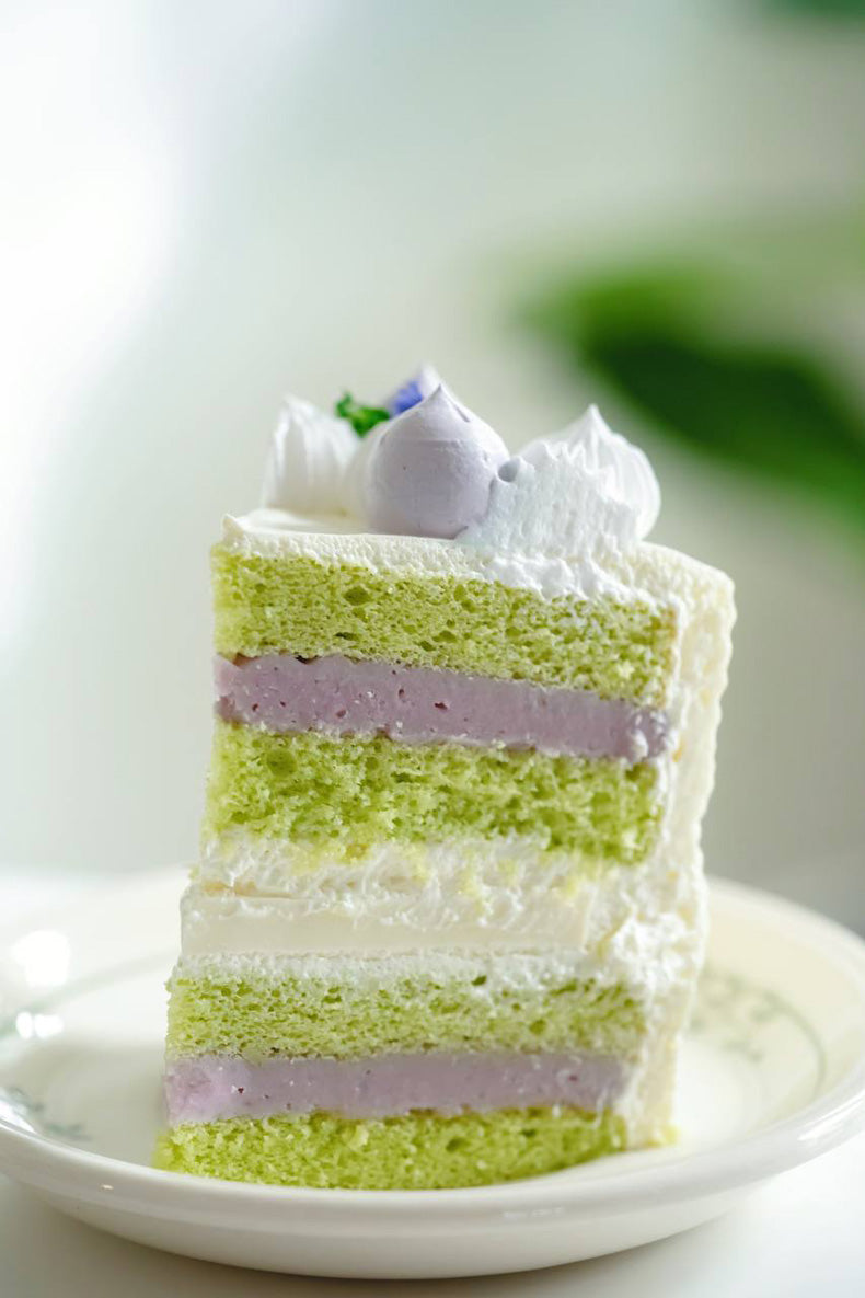 A slice of pandan sponge cake with pure taro filling, coconut jelly, taro jelly & Chantilly cream
